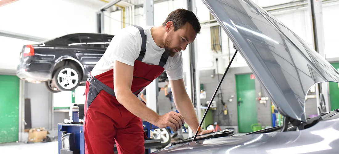 Mechaniker an offener Motorhaube bei der Inspektion und Wartung eines Fahrzeugs